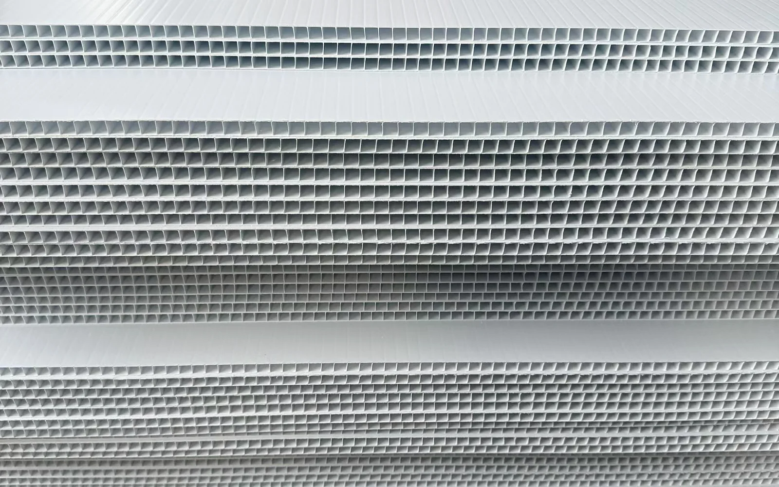 Stacked white corrugated plastic sheets showing the fluted edges